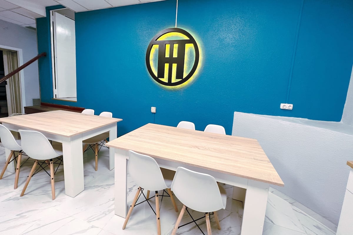 Une salle de conférence avec un mur bleu, un logo, ainsi que des chaises et des tables blanches.