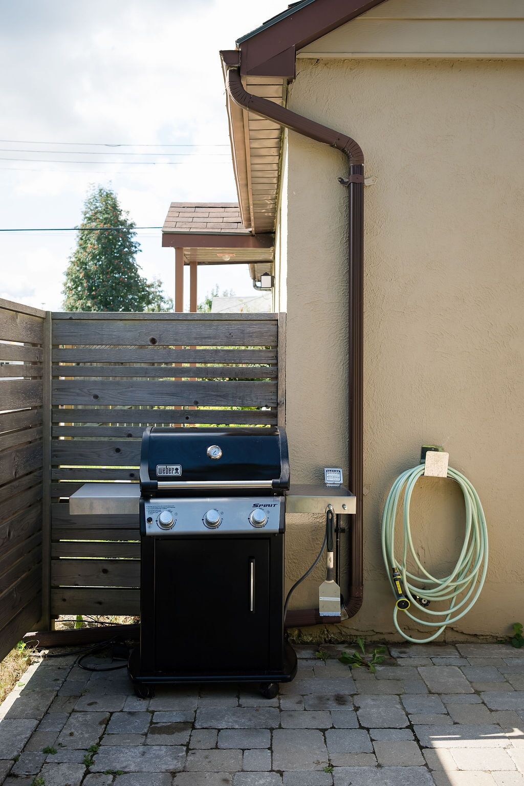 A Weber Spirit grill with a hose and a wooden fence in the background.
