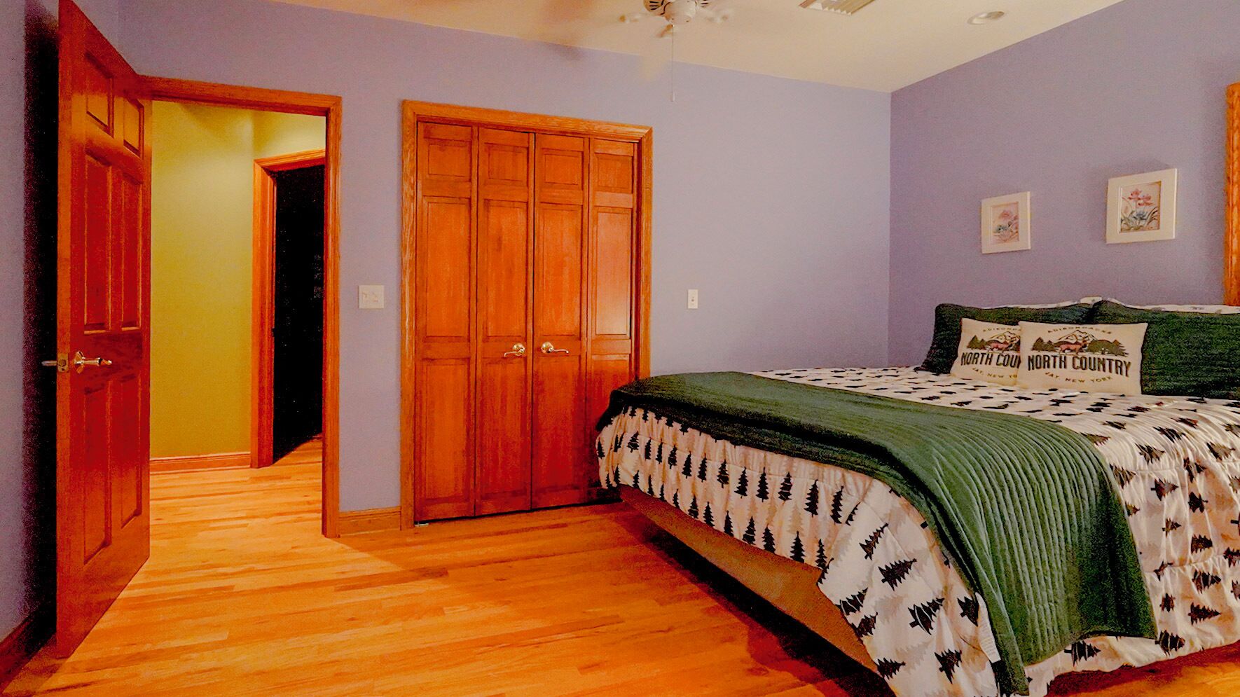 A bedroom with a wooden wardrobe, a bed with a patterned bedspread, and a hallway leading to another room.
