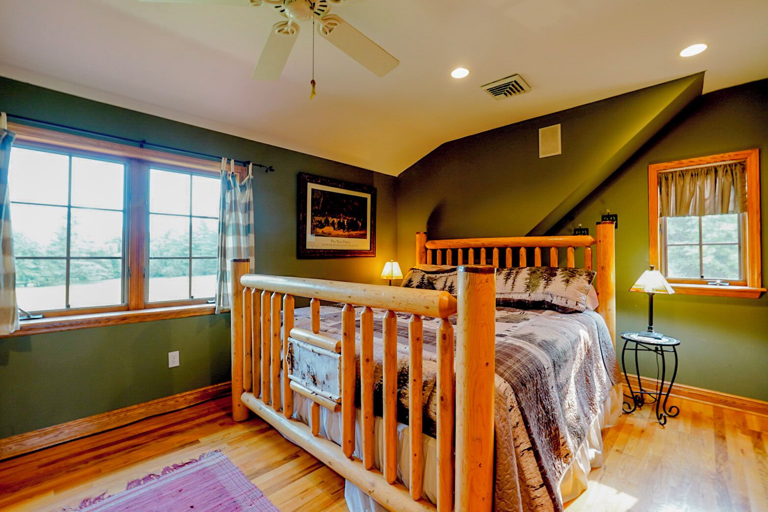 A bedroom with a wooden bed, a ceiling fan, a window with curtains, and a framed picture on the wall.