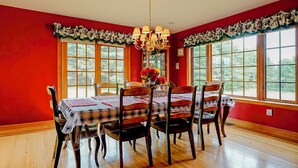 A dining room with a red wall, wooden floor, and a table set for six with plaid tablecloths. - Deer Haven Lodge on 16 acres with mountain views and fireplace (Jay)