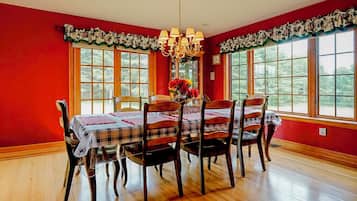 Une salle à manger avec un mur rouge, un plancher en bois et une table dressée pour six personnes, recouverte de nappes à carreaux.