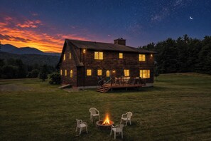 Une maison en bois dotée d’une terrasse et de meubles de jardin, entourée d’une pelouse et surplombant un ciel étoilé.