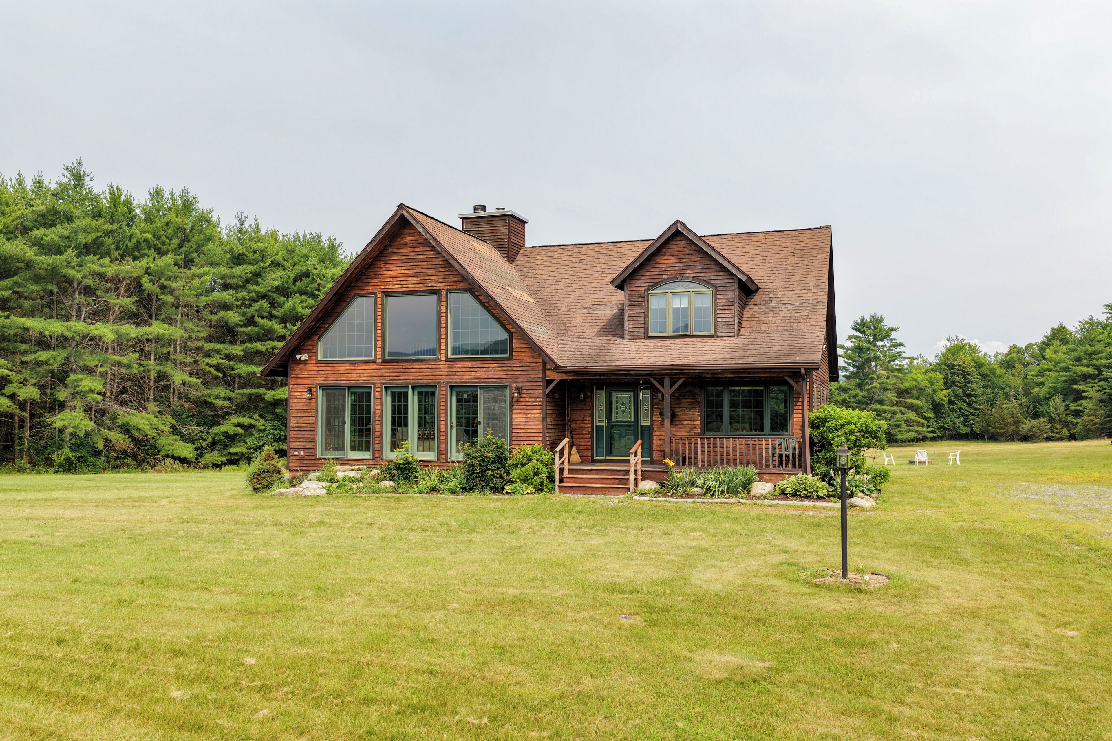 A two-story wooden cabin with a porch, large windows, and a grassy yard.