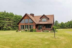 Une cabane en bois à deux étages, dotée d’un porche, de grandes fenêtres et d’une cour gazonnée.