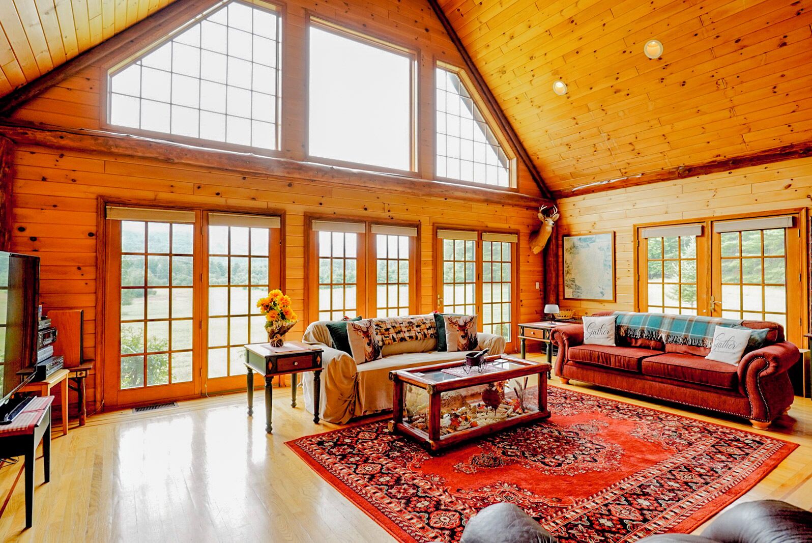 A spacious living room with large windows, a red sofa, a coffee table, and a fireplace.