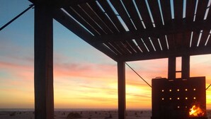 Una terraza de madera con un elemento decorativo de fuego, con vistas a una playa al atardecer.