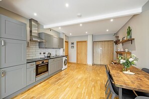Enjoy cooking in this well-equipped kitchen with an oven, stainless steel range hood, and wooden dining table.