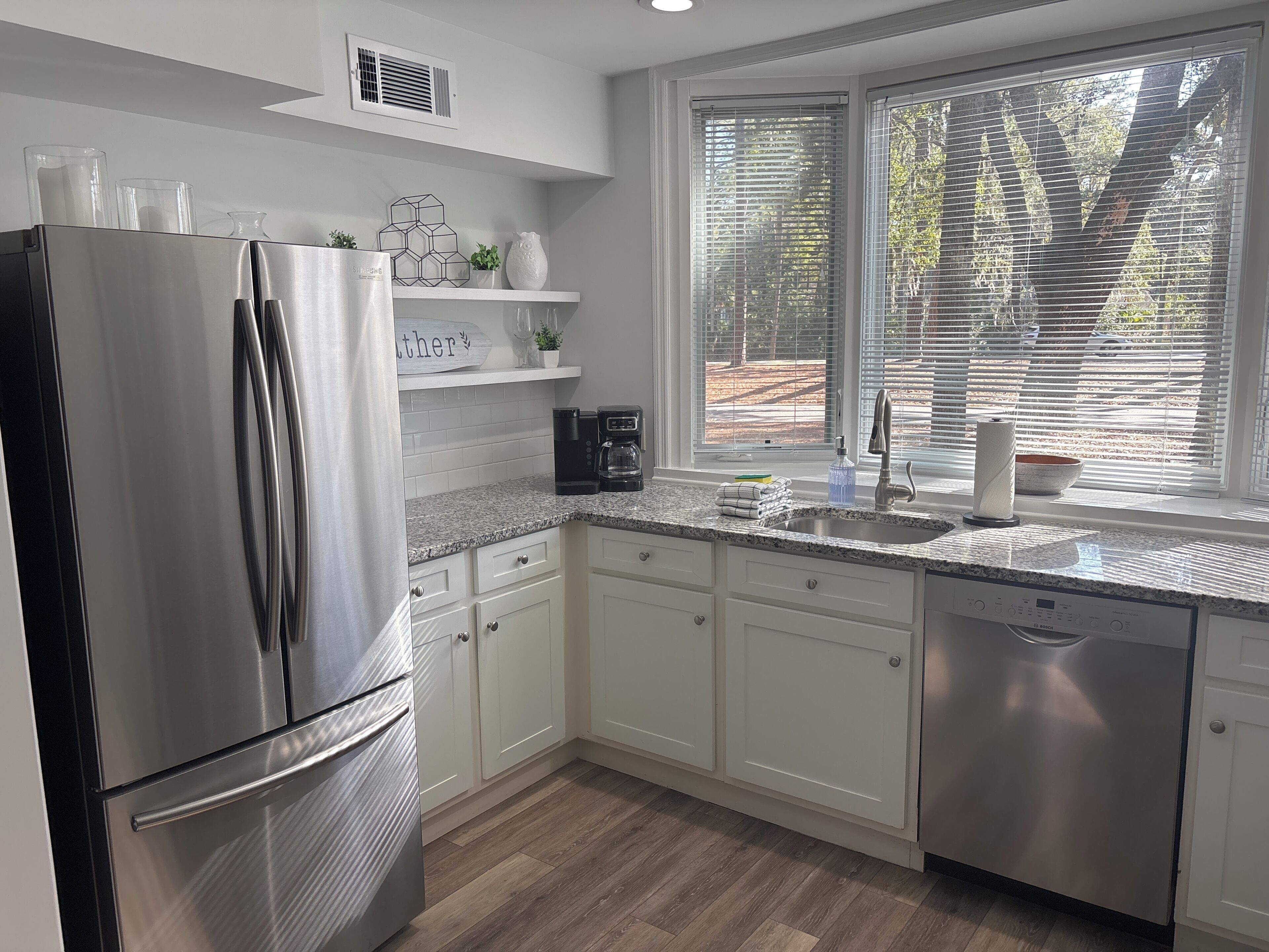 A modern kitchen with stainless steel appliances, white cabinetry, a granite countertop, and a window with blinds.