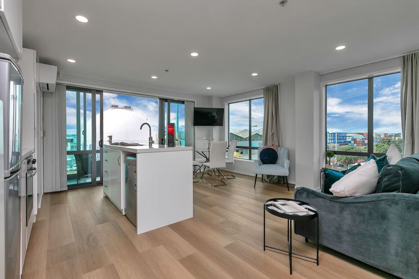 Un appartement moderne comprenant une cuisine, un coin repas et un salon, avec de grandes fenêtres offrant une vue sur la ville.