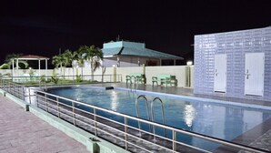 Une piscine dotée d’une rambarde en métal, d’un espace de repos couvert et d’un bâtiment dont l’extérieur est revêtu de carreaux.