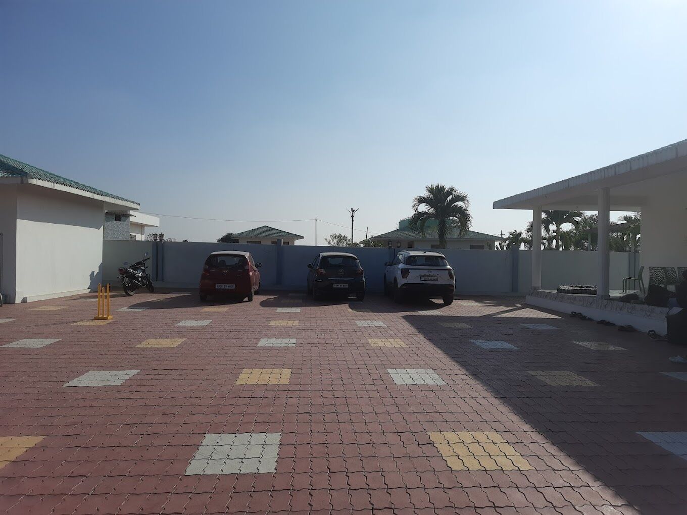 Un espace de stationnement avec trois voitures, un chemin piétonnier pavé et un bâtiment blanc doté d’un toit vert.