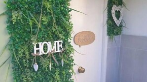 Une porte ornée d’un décor mural représentant des feuilles vertes, d’une enseigne indiquant « HOME », d’une autre indiquant « bonjour » et d’un décor en forme de cœur.