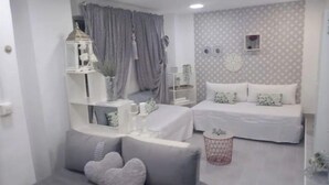 Une chambre moderne avec deux lits, un canapé gris et une petite table agrémentée d’objets décoratifs.