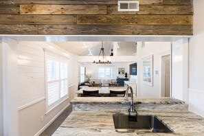 A kitchen with a marble countertop, a stainless steel sink, and wooden ceiling beams.