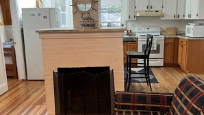 A living room with a plaid sofa, a fireplace, and a kitchen in the background. - Classic Old Orchard Beach Cottage One Block from the Beach (Old Orchard Beach)