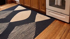 A kitchen with wooden cabinets, a white stove, a sink, and a patterned rug. - Classic Old Orchard Beach Cottage One Block from the Beach (Old Orchard Beach)