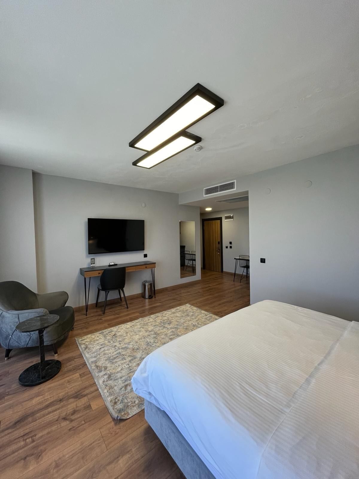 Una habitación de hotel moderna con una cama grande, un escritorio con una silla, un televisor y un pequeño rincón de descanso.