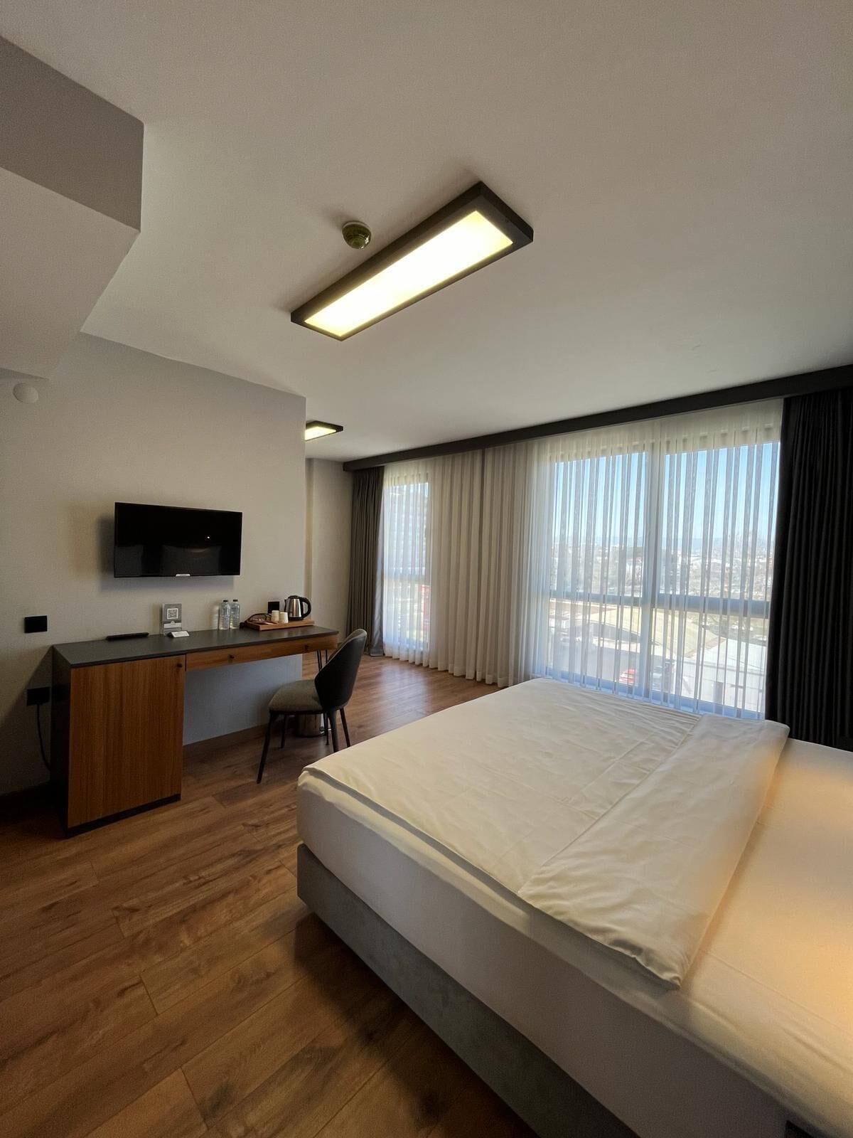 A hotel room with a bed, a desk, a chair, a television, and a window with curtains.