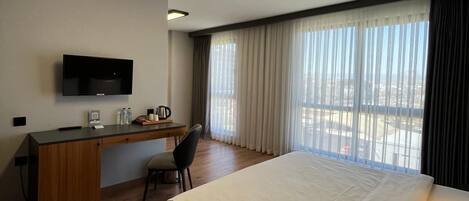 A hotel room with a bed, a desk, a chair, a television, and a window with curtains.