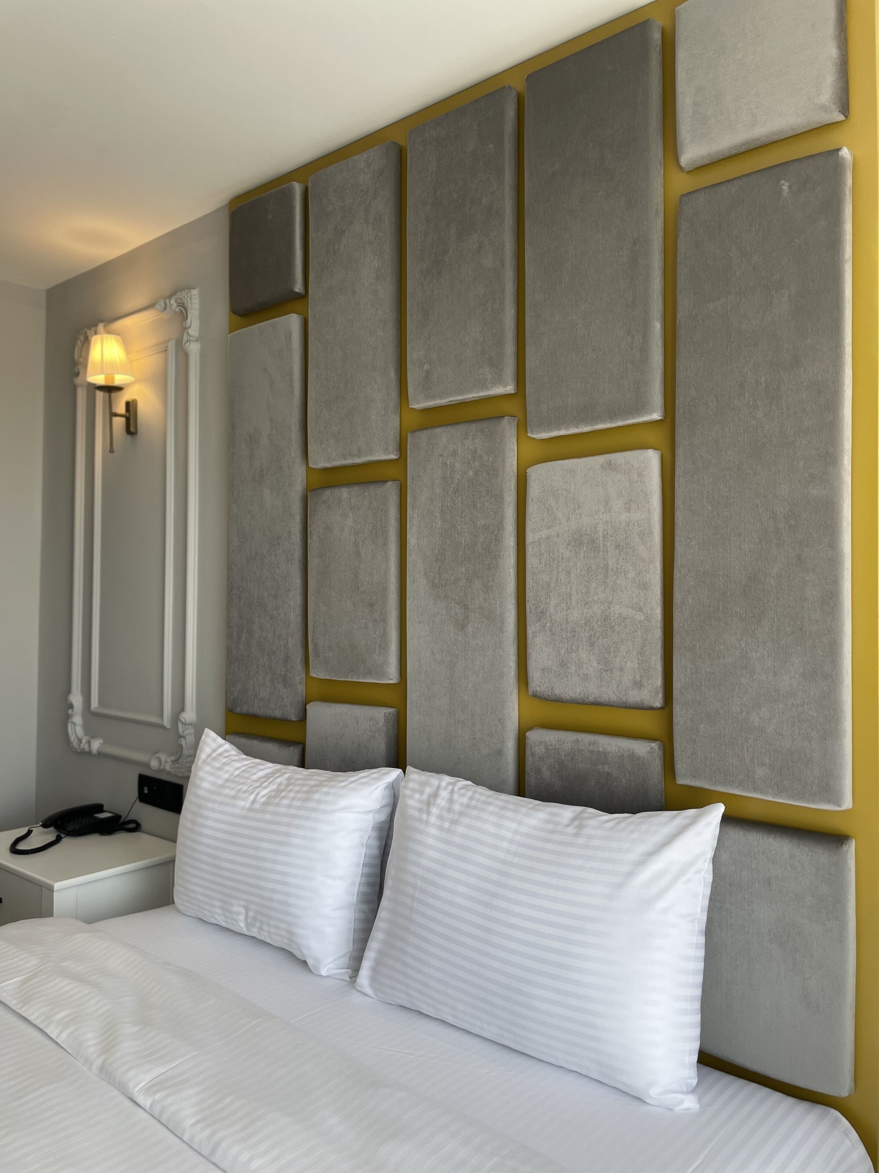 A hotel room with a large bed, a bedside table with a lamp, and a wall with a geometric pattern.