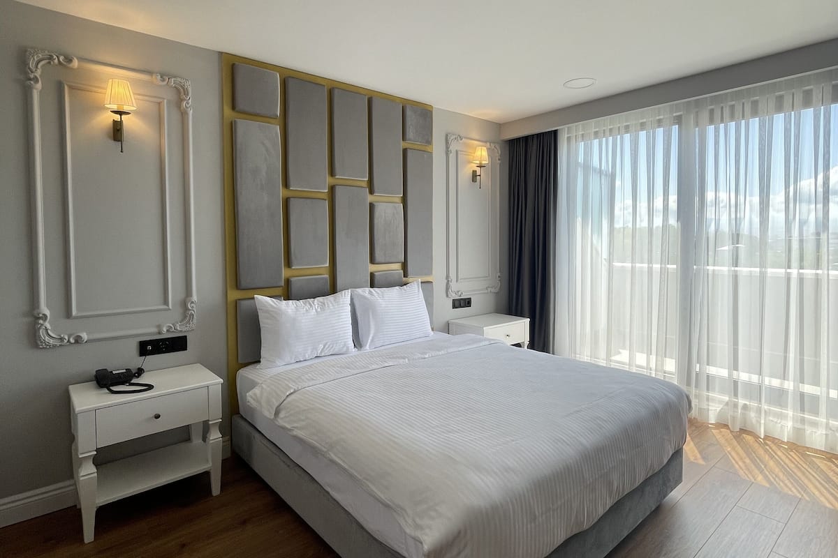 Ein modernes Schlafzimmer mit einem großen Bett, einem Nachttisch, einer Wandlampe und einem großen Fenster mit durchsichtigen Vorhängen.