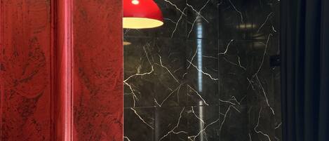 Un baño con una bañera independiente, una lámpara colgante roja y una pared de mármol con vetas blancas.
