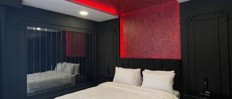 A modern bedroom with a large bed, a red accent wall, and a window with a view.