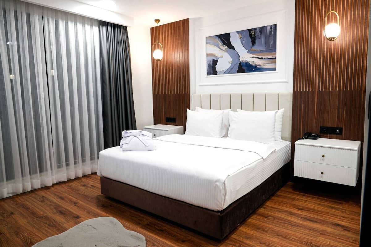 Ein modernes Hotelzimmer mit einem großen Bett, Holzboden, einem weißen Nachttisch und einem Bild an der Wand.