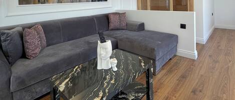 A modern living room with a grey sectional sofa, a marble coffee table, and a large abstract painting on the wall.