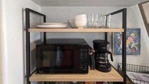 A kitchen area with a microwave, coffee maker, and shelves holding plates and glasses. - UofA Tiny House + Fire Pit (Tucson)