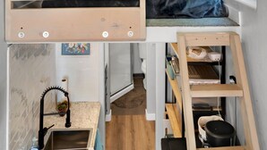 A compact studio apartment with a bunk bed, kitchenette, and a small window. - UofA Tiny House + Fire Pit (Tucson)