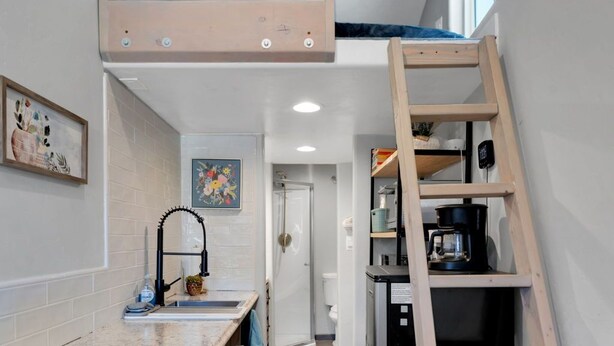 A compact kitchen with a built-in bench, a ladder, and a refrigerator. - UofA Tiny House + Fire Pit (Tucson)