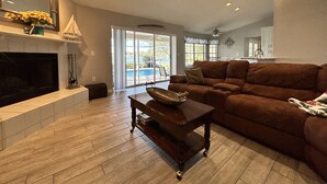 A spacious living room with a fireplace, a large brown sofa, a wooden coffee table, and a ceiling fan.