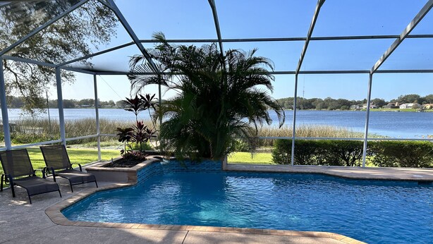 A pool area with a covered section, lounge chairs, and a view of a lake.