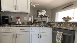 A modern kitchen with white cabinets, a granite countertop, a built-in dishwasher, and a ceiling fan.