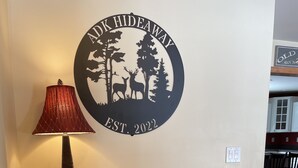 Un meuble en bois avec des tiroirs, une lampe et un autocollant mural représentant des cerfs et des arbres.