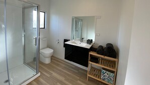 A modern bathroom with a glass shower enclosure, a white toilet, a sink with a mirror, and a shelf with towels.