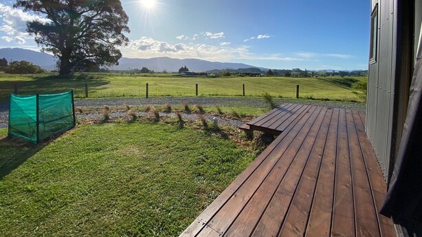 A wooden deck with a view of a grassy field and a tree, under a clear sky.