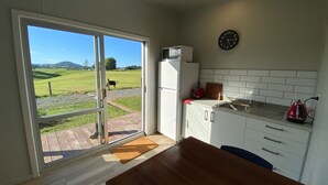 A kitchen with a view of a green field and a cow, a refrigerator, a sink, and a clock on the wall.
