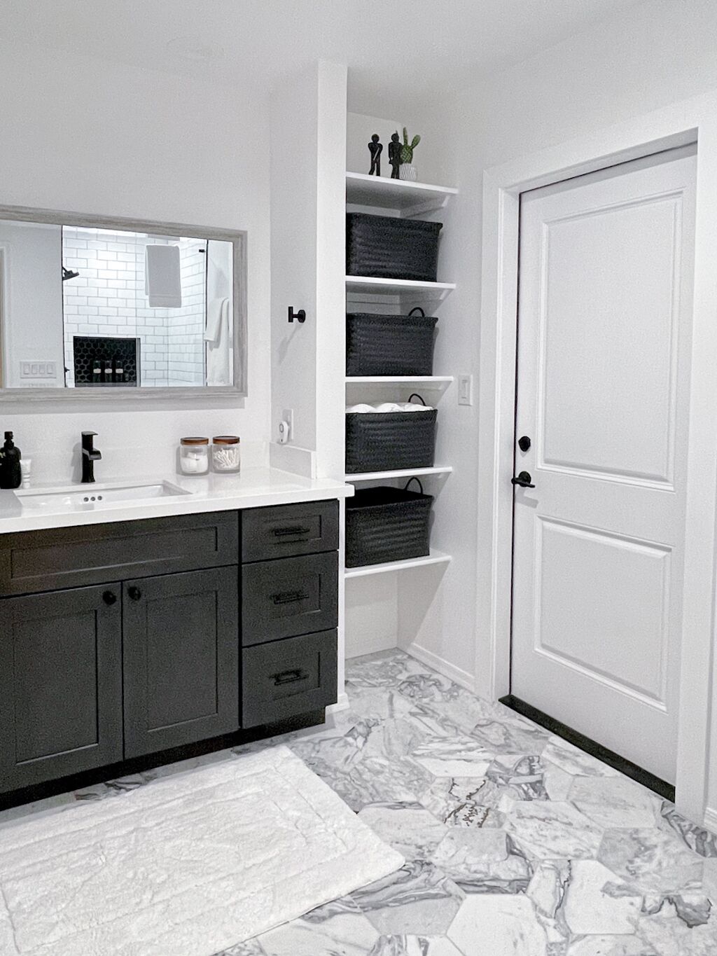 A bathroom with a white vanity, dark cabinets, a marble floor, and a white door.
