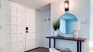 A hallway with a wooden floor, a white door, a round mirror, a wall-mounted lamp, and two woven baskets on a console table. - Modern Home with Private Pool (Phoenix)