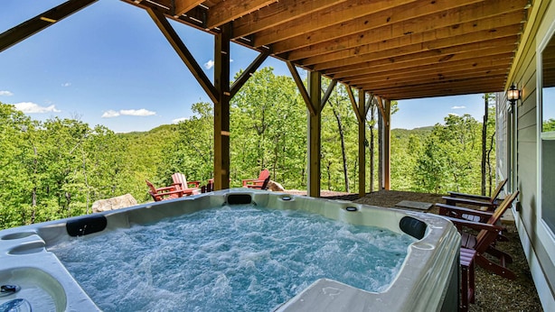 Un bain à remous sous une pergola en bois, avec vue sur un paysage boisé.