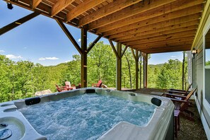 Una vasca idromassaggio sotto un pergolato in legno, con vista su un paesaggio boschivo.