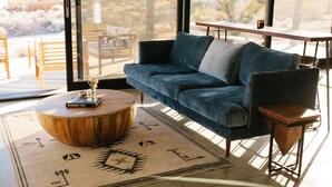 A modern living room with a blue sofa, a wooden coffee table, and a view of a desert landscape through large windows. - Joshua Tree Monochrome - 5 mins from National Park (Joshua Tree)