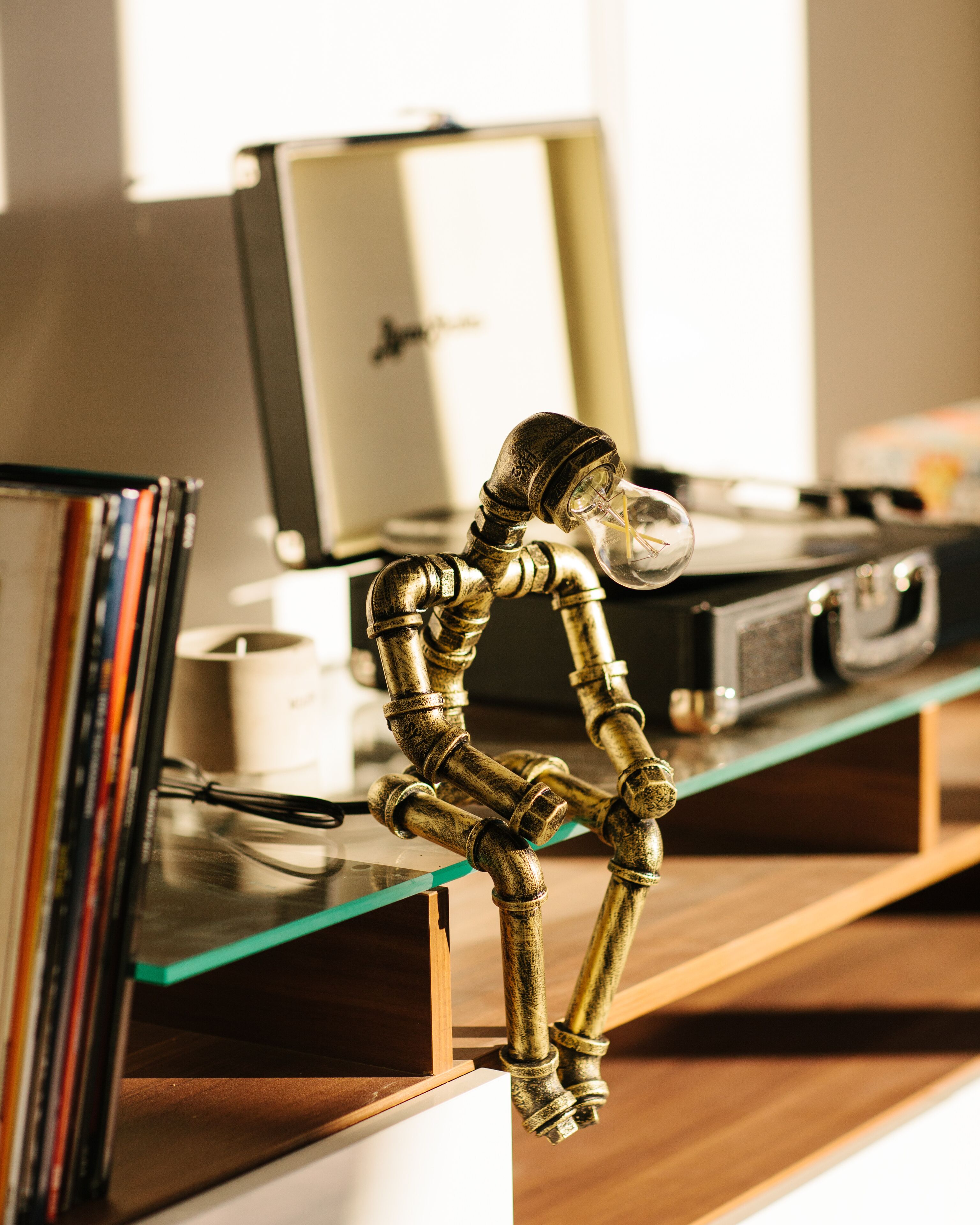A brass skeleton figure on a glass shelf with books and a record player in the background.