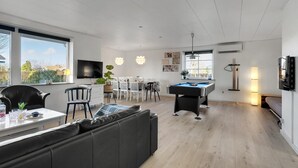 Ein modernes Wohnzimmer mit Poolbillard, einer Couch und einem Essbereich mit Fernseher.