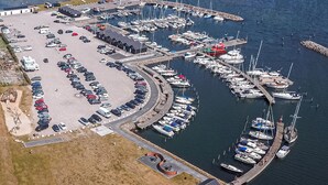 Ein Luftbild eines Yachthafens mit vertäuten Booten, einem Parkplatz und einem Gebäude mit geneigtem Dach.