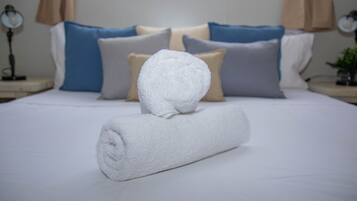 A neatly made bed with white linens, a rolled towel, and a variety of pillows in different colors.