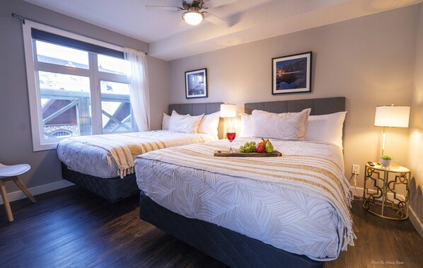 Habitación de hotel con dos camas, una ventana con cortinas, una mesita con lámpara y un cuadro enmarcado en la pared.
